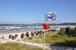Rote Badeverbots-Flagge am Strand. Das Meer im Hintergrund schlägt starke Wellen.
