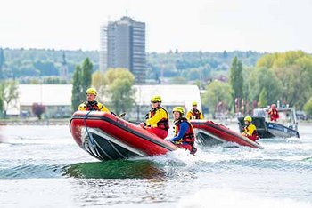 Mehrere Personen mit Einsatzkleidung in Booten auf Wasser