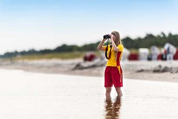 Rettungsschwimmerin schaut mit einem Fernglas auf das Wasser.