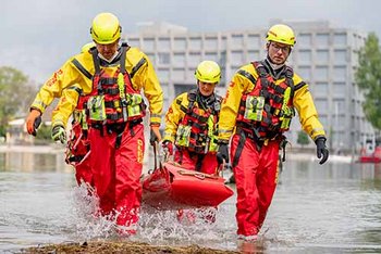 Mehrere Personen in rot-gelber Einsatzkleidung schleppen Trage ans Ufer