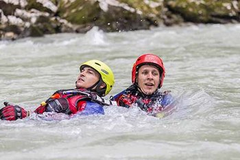 Zwei Strömungsretter mit Helmen und blau-roter Einsatzkleidung im Wasser