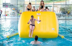Kinder rutschen von dem Fitnass-Parkour ins Wasser.