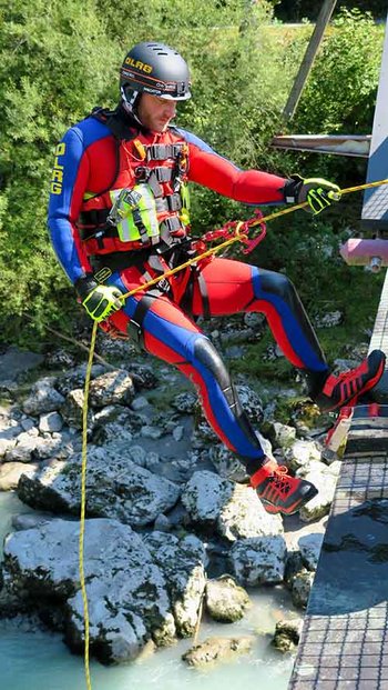 Strömungsretter mit Helm und rot-blauer Einsatzkleidung seilt sich über Gewässer von Brücke ab