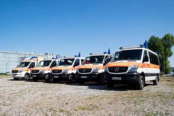 Mehrere Einsatzfahrzeuge stehen in Reihe nebeneinander auf Schotter vor blauem Himmel