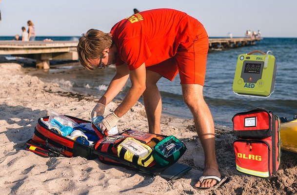 Ein junger Mann greift in seinen Sanitätsrucksack, der am Strand liegt. 