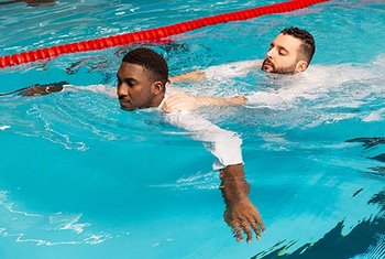 Bekleidete Personen bei einer Rettungsübung auf dem Bauch im Schwimmbecken.