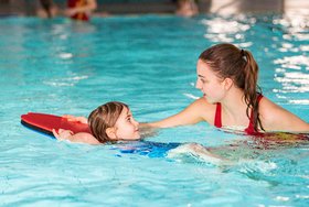 Die DLRG Rettungsschwimmerin hilft einem Kind mit einem Kickboard über das Wasser zu treiben