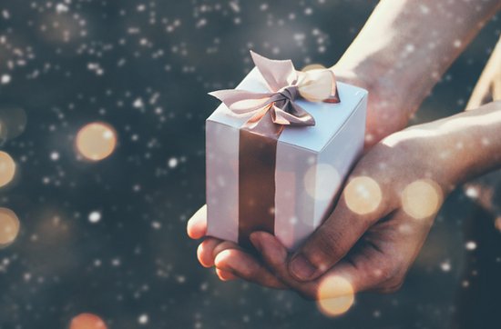 Hände, die ein kleines weißes Geschenk in der Hand halten. Weihnachtlicher Hintergrund mit Sternen.