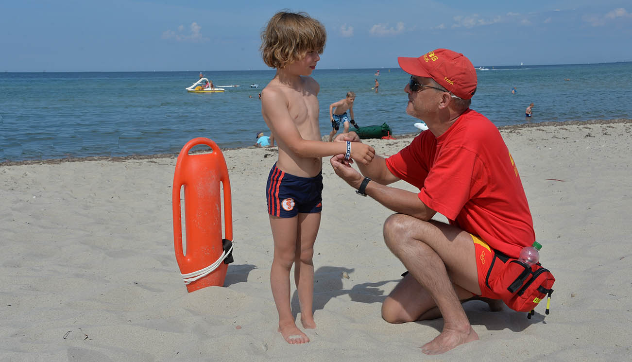 Älterer Rettungsschwimmer mit kleinem Jungen am Strand.